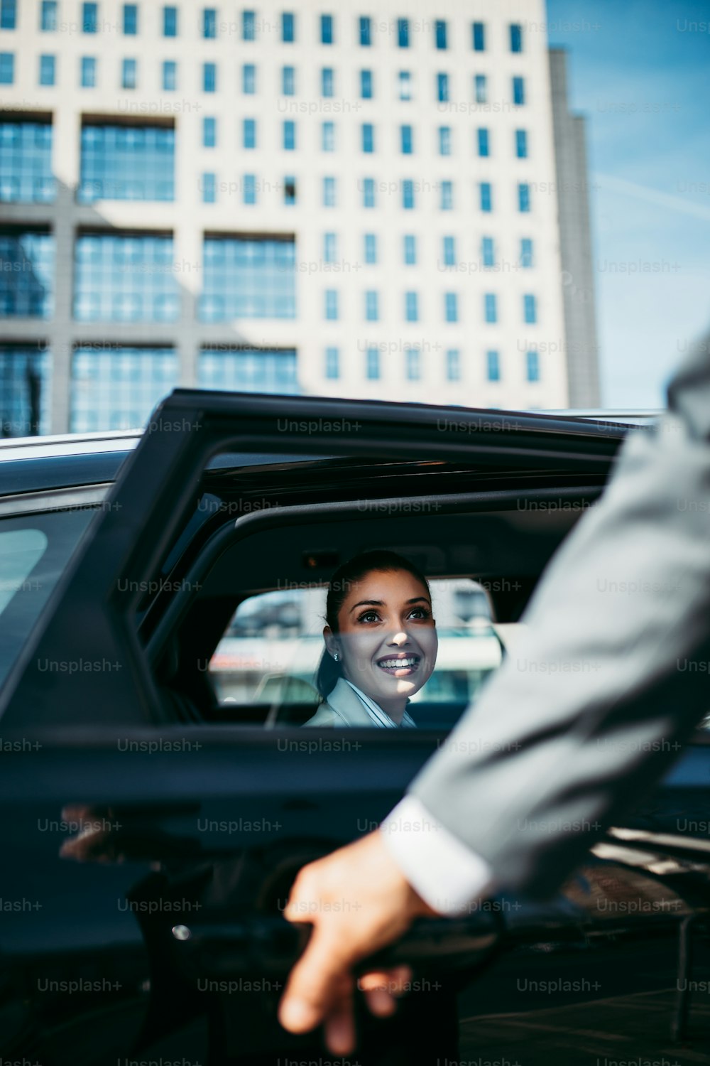 Boa aparência jovem mulher de negócios sentada no banco de trás no carro de luxo. Ela usando seu smartphone, sorrindo e olhando para fora. Transporte no conceito de negócio corporativo.