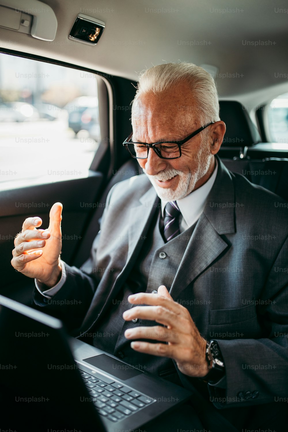 Uomo d'affari anziano di bell'aspetto seduto sul sedile posteriore in auto di lusso. Usando il suo laptop e reagendo emotivamente. Il trasporto nel concetto di business aziendale.