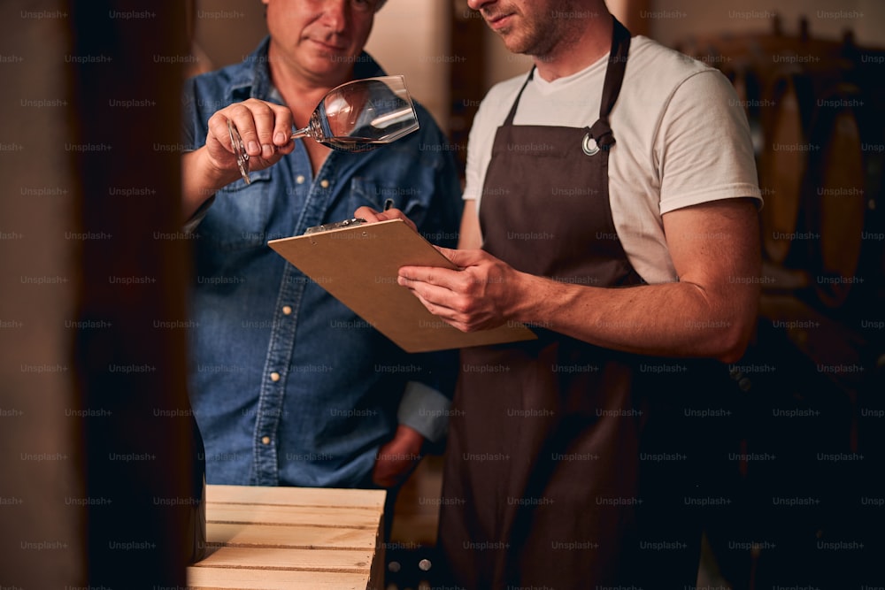 Cropped photo of two unrecognized sommeliers making notes about the quality of wine in a cellar