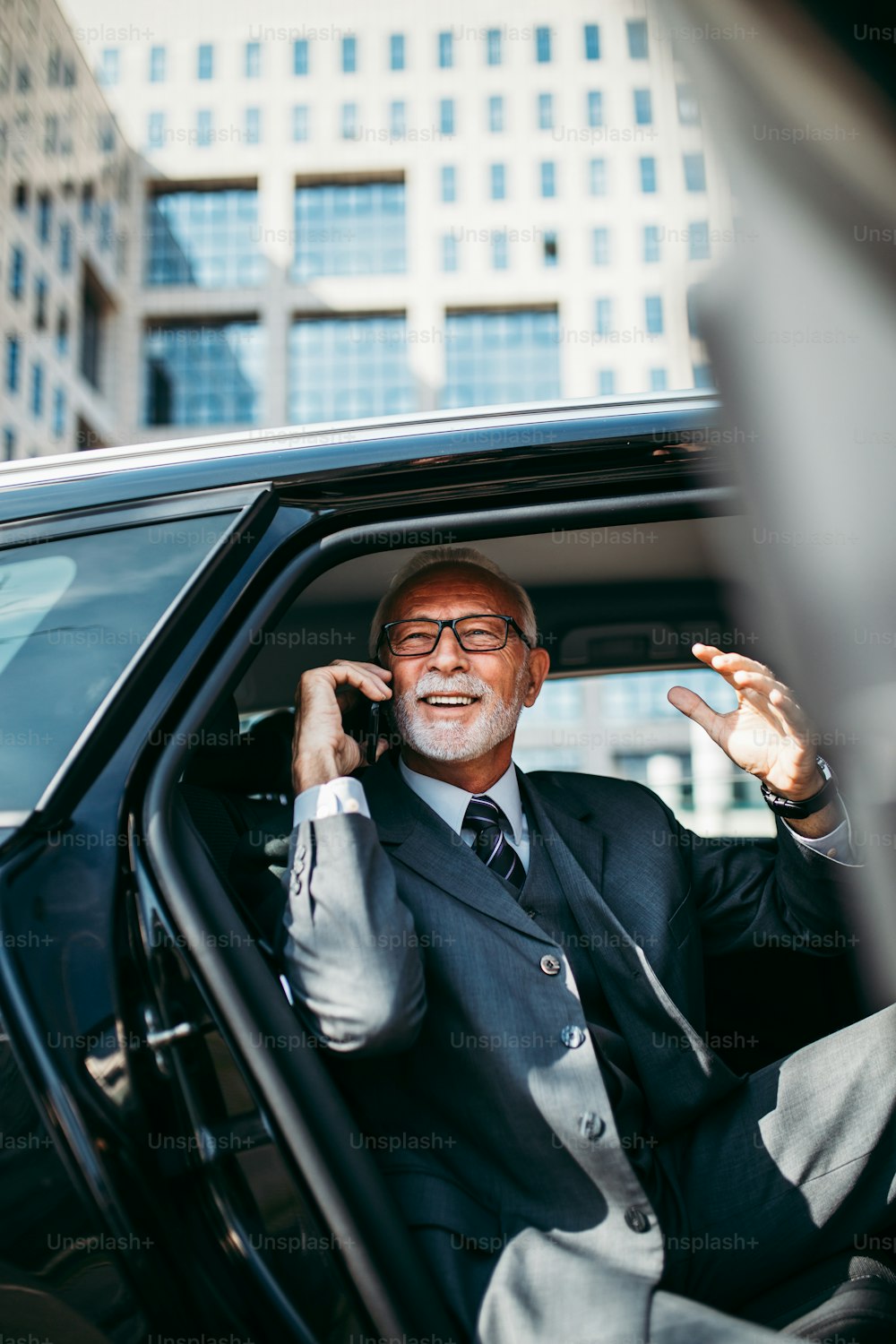 Hombre de negocios senior de buen aspecto sentado en el asiento trasero en un automóvil de lujo. Abre las puertas del coche y sale o sale. Gran negocio que se construye en el fondo. El transporte en el concepto de negocio corporativo.