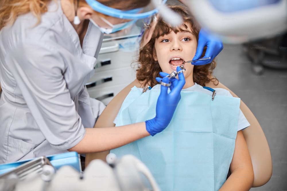 Dentista pediátrico usando una jeringa para el niño mientras le administra anestesia local