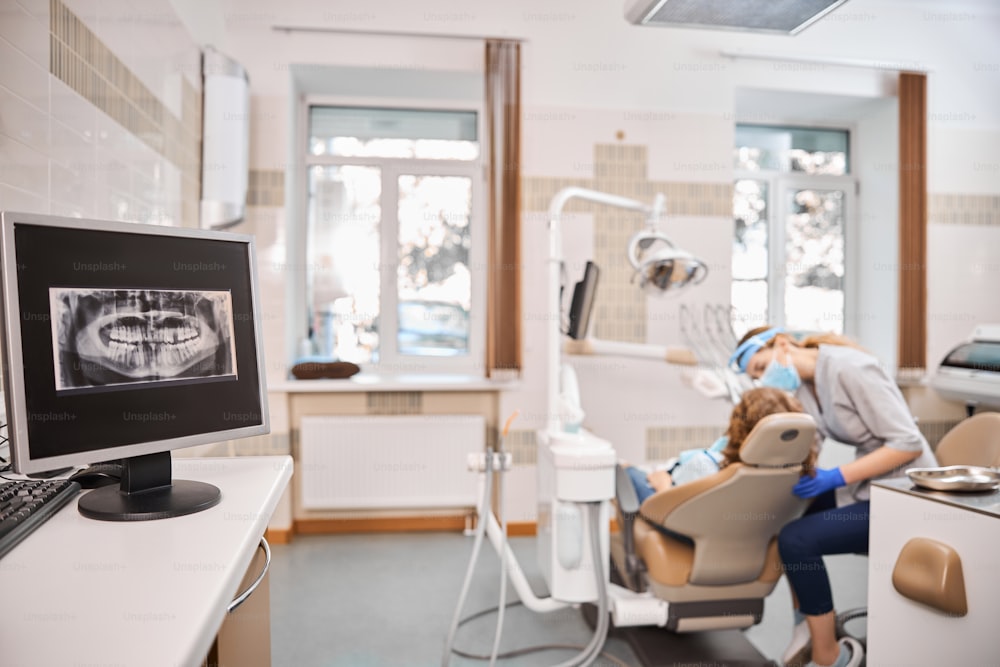 Foto de um consultório odontológico com todos os equipamentos e aparelhos odontológicos e um grande raio-x na tela do computador