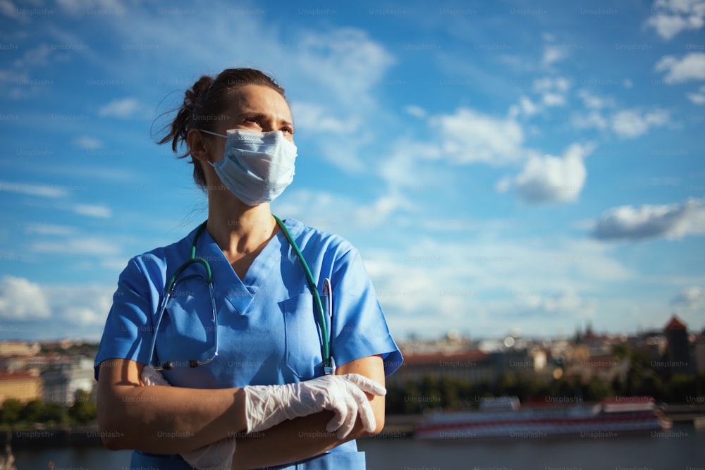 코로나 바이러스 전염병. 청진기, 의료용 마스크, 고무 장갑을 끼고 하늘을 배경으로 먼 거리를 바라보는 자신감 넘치는 현대 의사 여성.