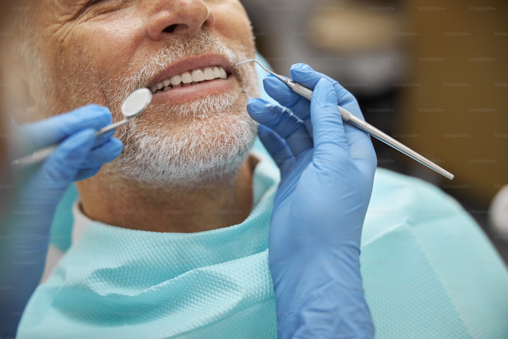 Photo recadrée d’une personne âgée souriante tout en faisant examiner ses dents par un dentiste