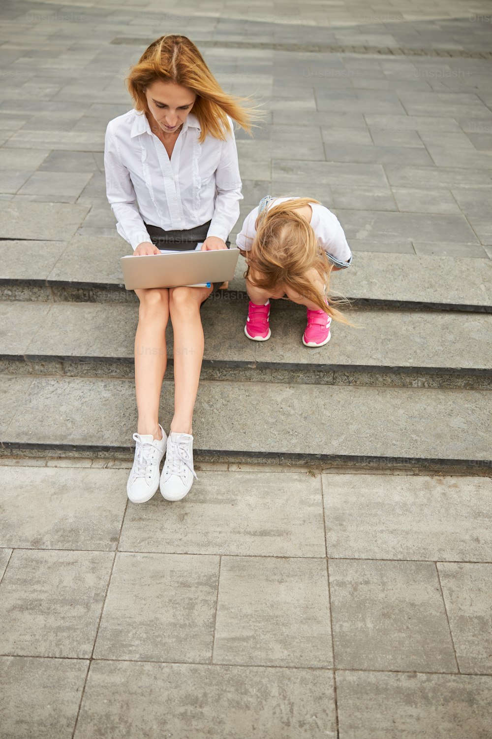 屋外の階段に座りながら母親を待っている若いかわいい女性の子供