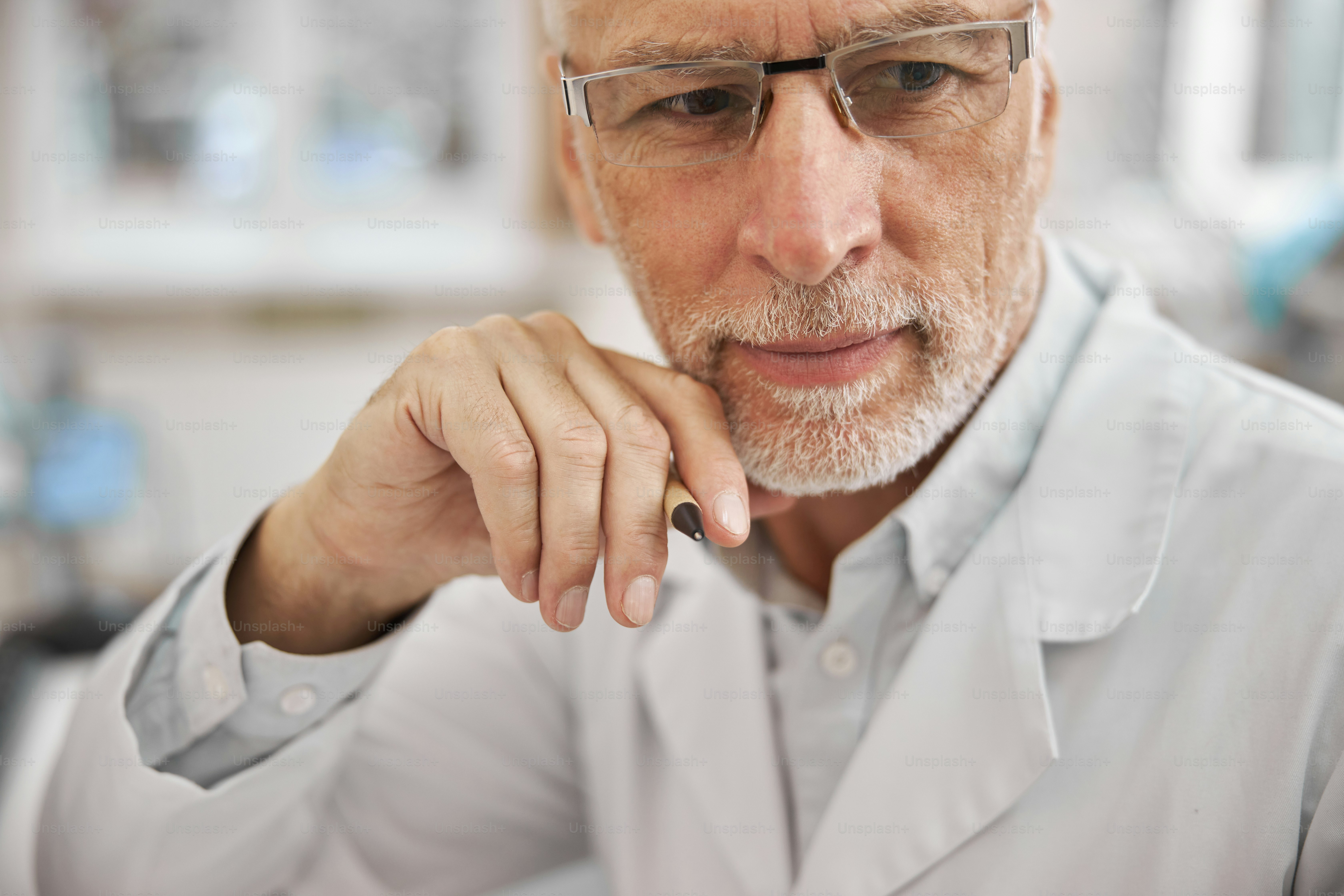 Close-up photo of an elderly healthcare worker wearing a lab coat and looking thoughtful