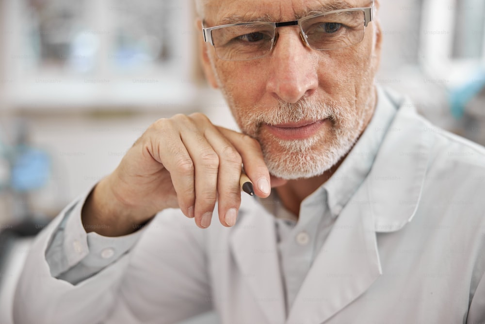 Close-up photo of an elderly healthcare worker wearing a lab coat and looking thoughtful