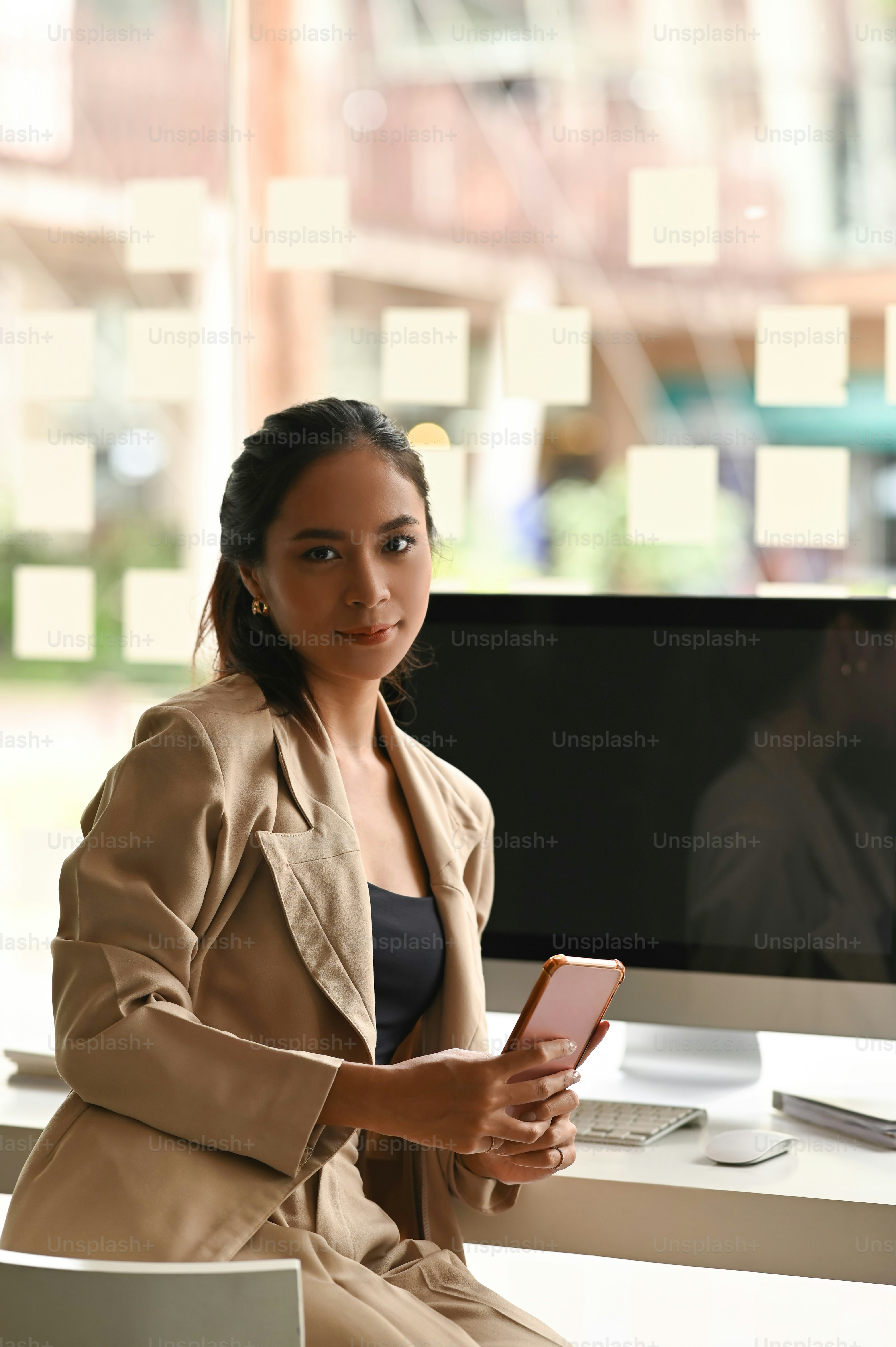 Una mujer sostiene un teléfono inteligente en las manos mientras está sentada frente a una computadora en la sala de estar.