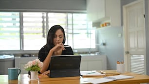 Una joven está usando una tableta de computadora mientras está sentada en una mesa de madera.