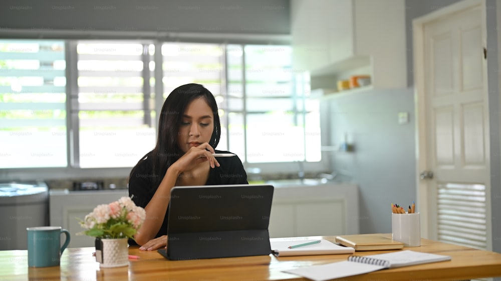 A young woman is using a computer tablet while sitting at a wooden table.