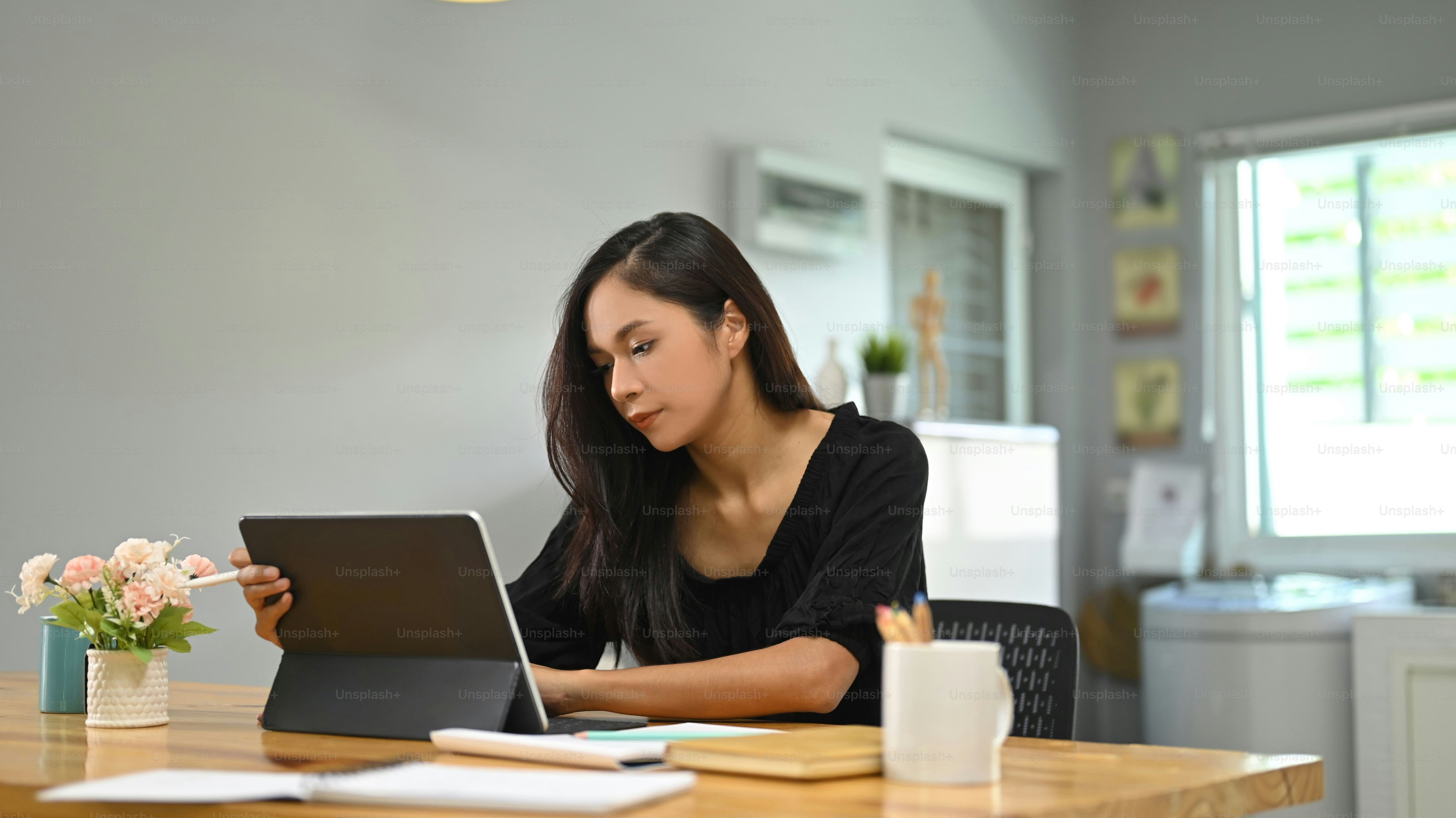 A young woman is using a computer tablet while sitting at a wooden ...