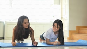 A young mother and daughter are doing an exercise together on the rubber mat.