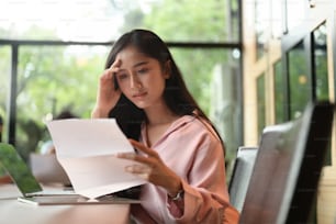 Una mujer estresada se lleva las manos a la cabeza mientras lee el papeleo en la sala de reuniones.