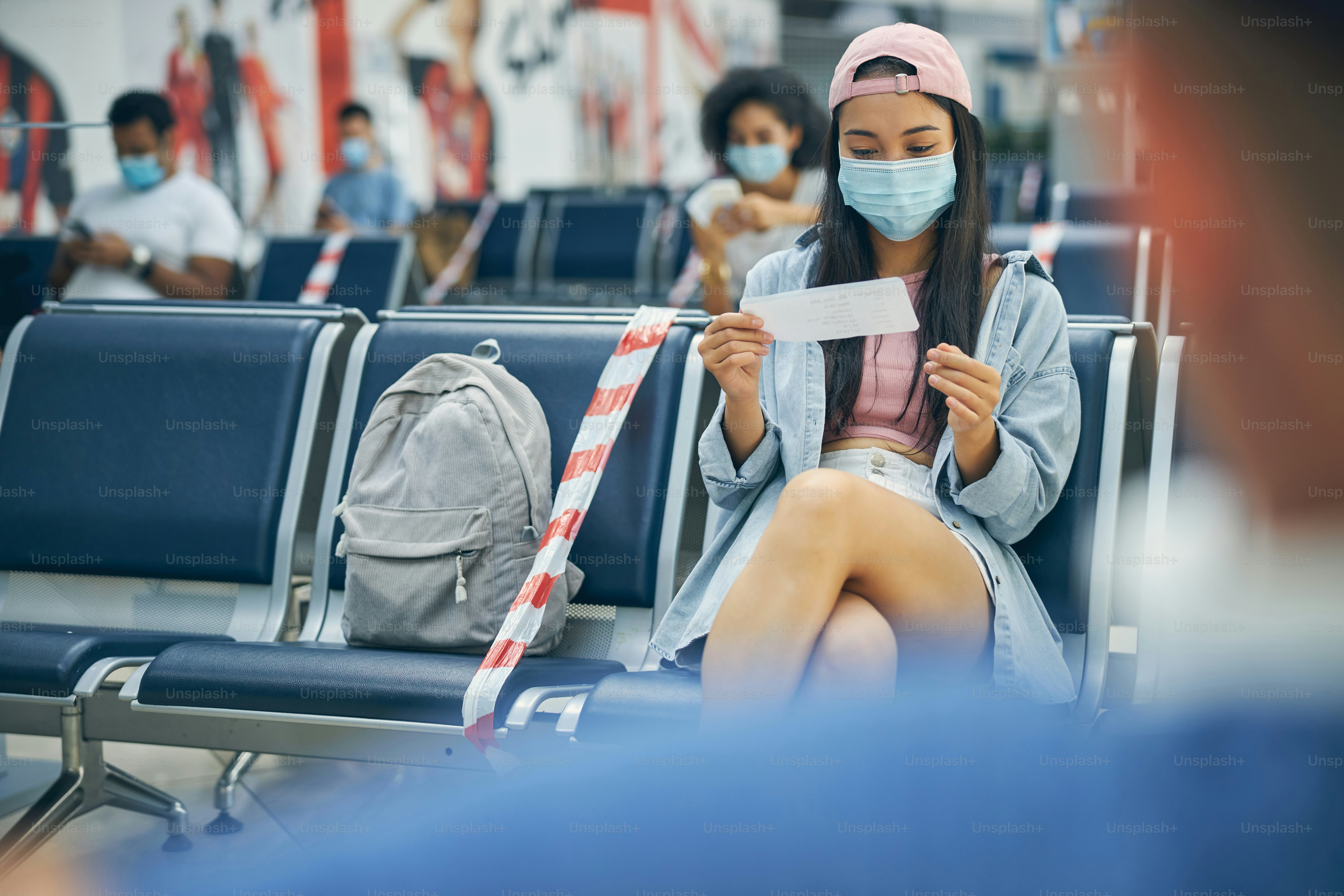 Stylish young female looking at the ticket while waiting for the catch a flight on the bench in the international airport