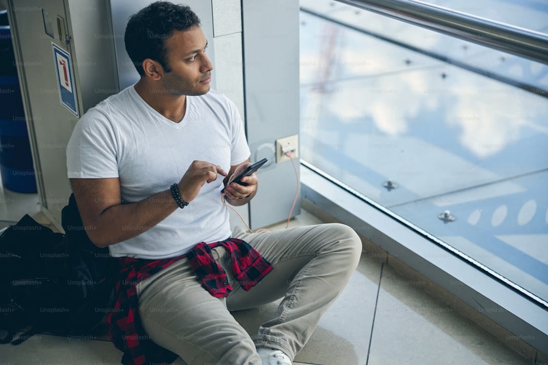 Side view portrait of Indian bright man looking out the window while holding mobile phone in hands