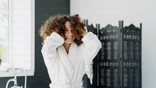 Beauty and wellness concept. Panoramic view of happy young adult afro american woman in bathrobe spending morning in bathroom, holding hands near curly wavy hair