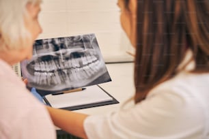 Vista posterior del médico profesional que muestra la imagen de los dientes sanos para el paciente de la anciana en la clínica dental