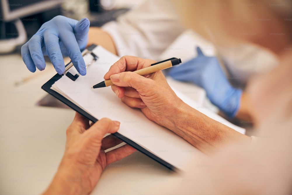 Close up portrait of doctor clipboard while elderly patient writing something after procedure of modern clinic