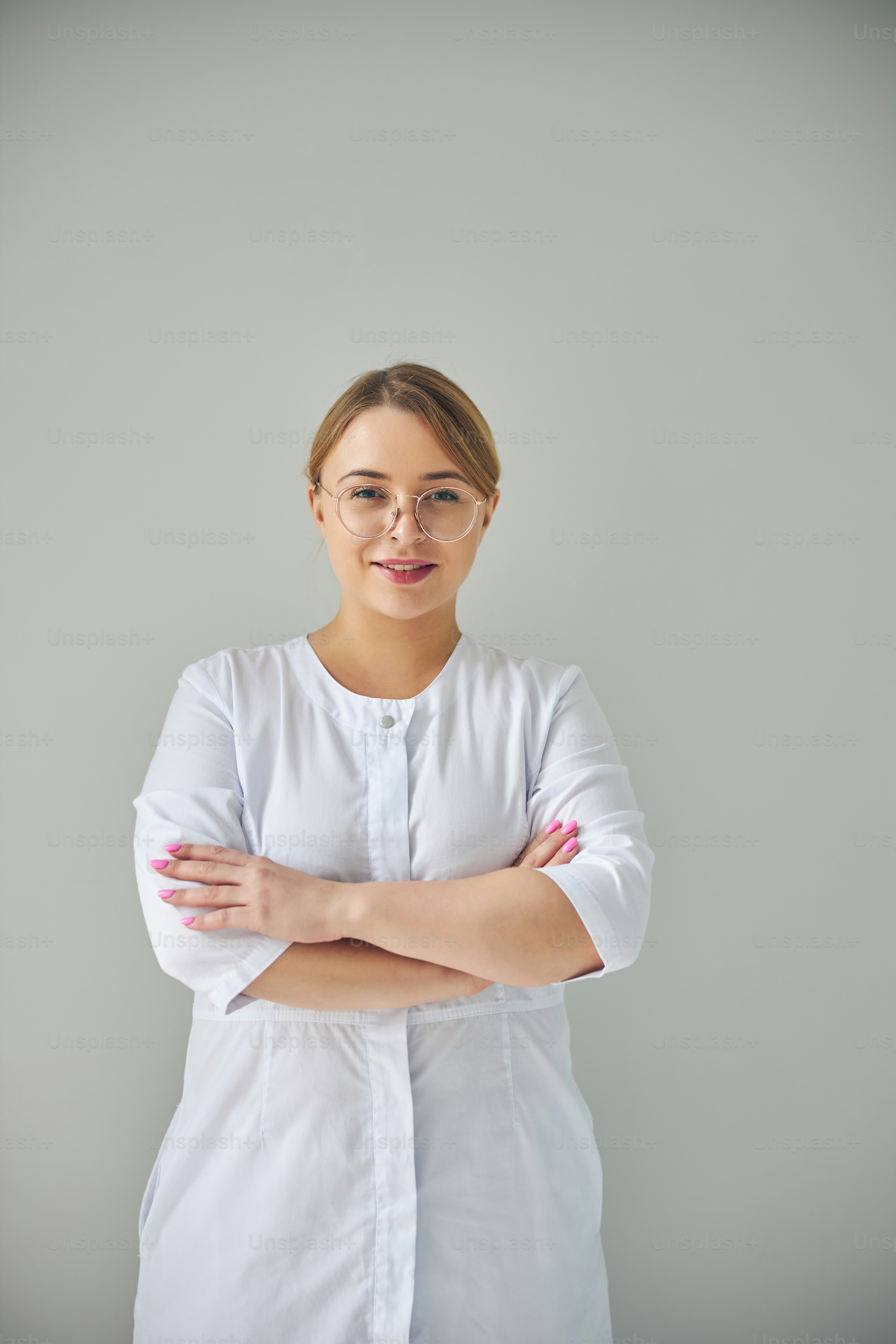 Front view of a blonde young lady doctor in round eyeglasses smiling at the camera