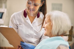 Portrait of professional cheerful woman doctor in protective mask talking with her female client on her clinic