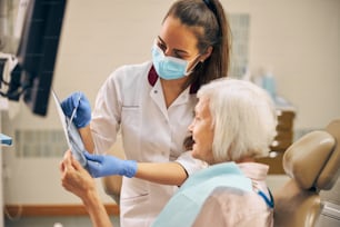 Dentista profesional hablando con su paciente anciana apoyándola antes de comenzar los procedimientos dentales en la clínica