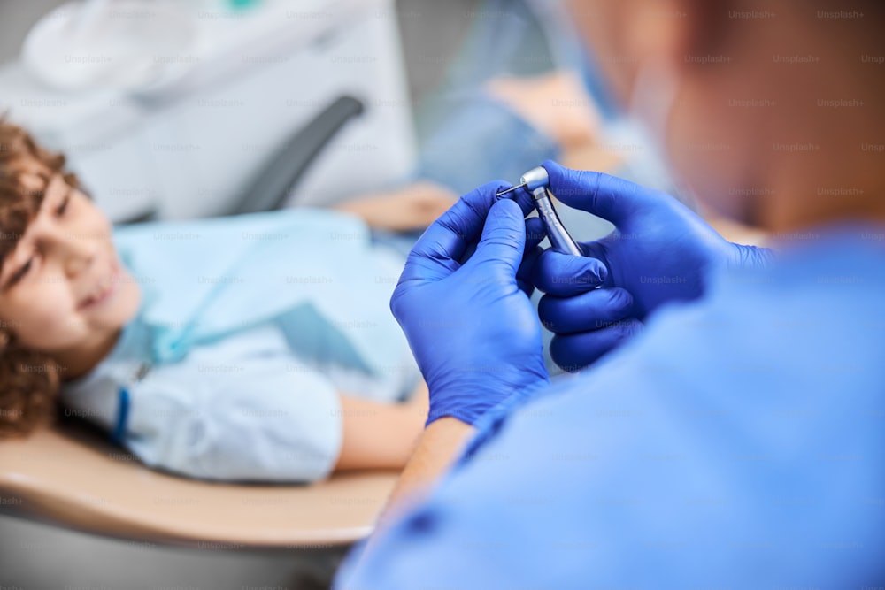 Foto em close-up do dentista usando luvas cirúrgicas e segurando uma broca dentária se preparando para o tratamento odontológico
