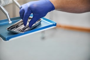 Foto recortada de la mano de los médicos con un guante quirúrgico azul recogiendo una herramienta dental de acero inoxidable de una caja