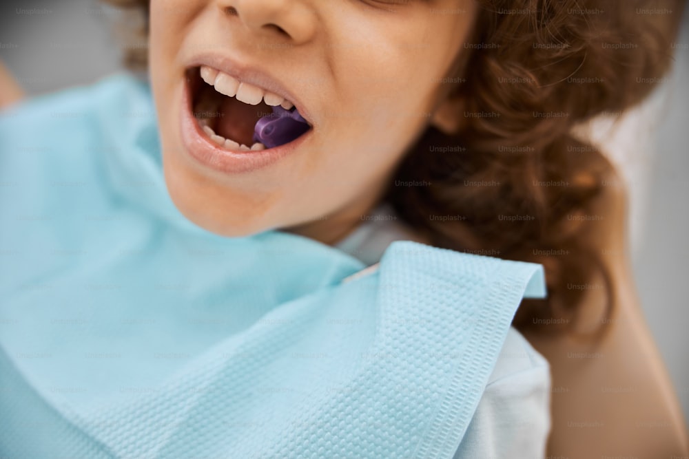 Foto em close-up de um menino bonito em uma cadeira odontológica tendo sua boca aberta com um bloco de mordida dentro