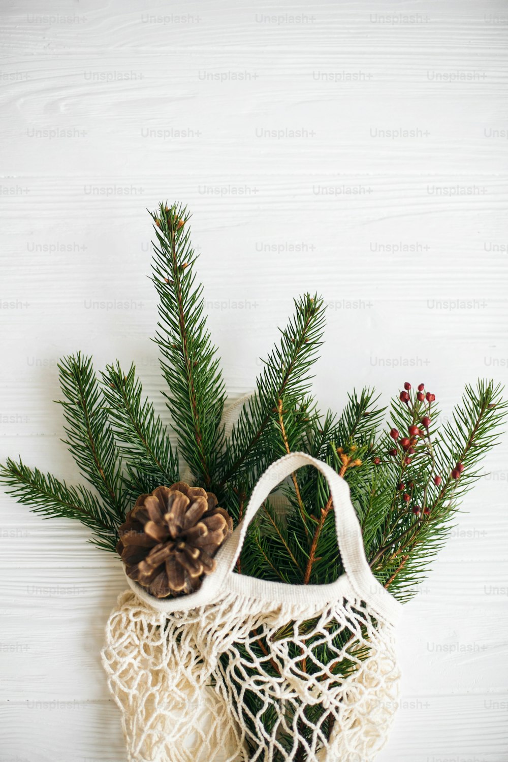 Reusable cotton bag with green spruce branches and pine cones on white rustic background. Net shopping bag with winter decorations, zero waste holidays. Top view with space for text