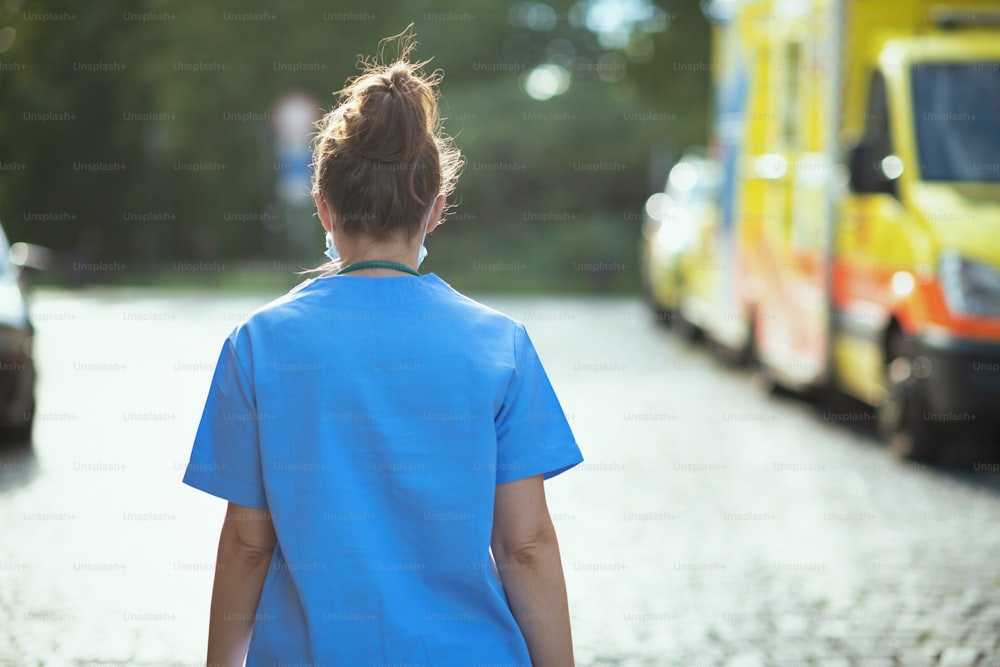 Pandemia di COVID-19. Visto da dietro la donna medico in camice all'esterno vicino all'ambulanza che cammina.
