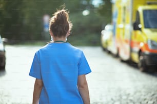 COVID-19-Pandemie. Von hinten gesehen Ärztin Frau in Peelings draußen in der Nähe von Krankenwagen gehen.