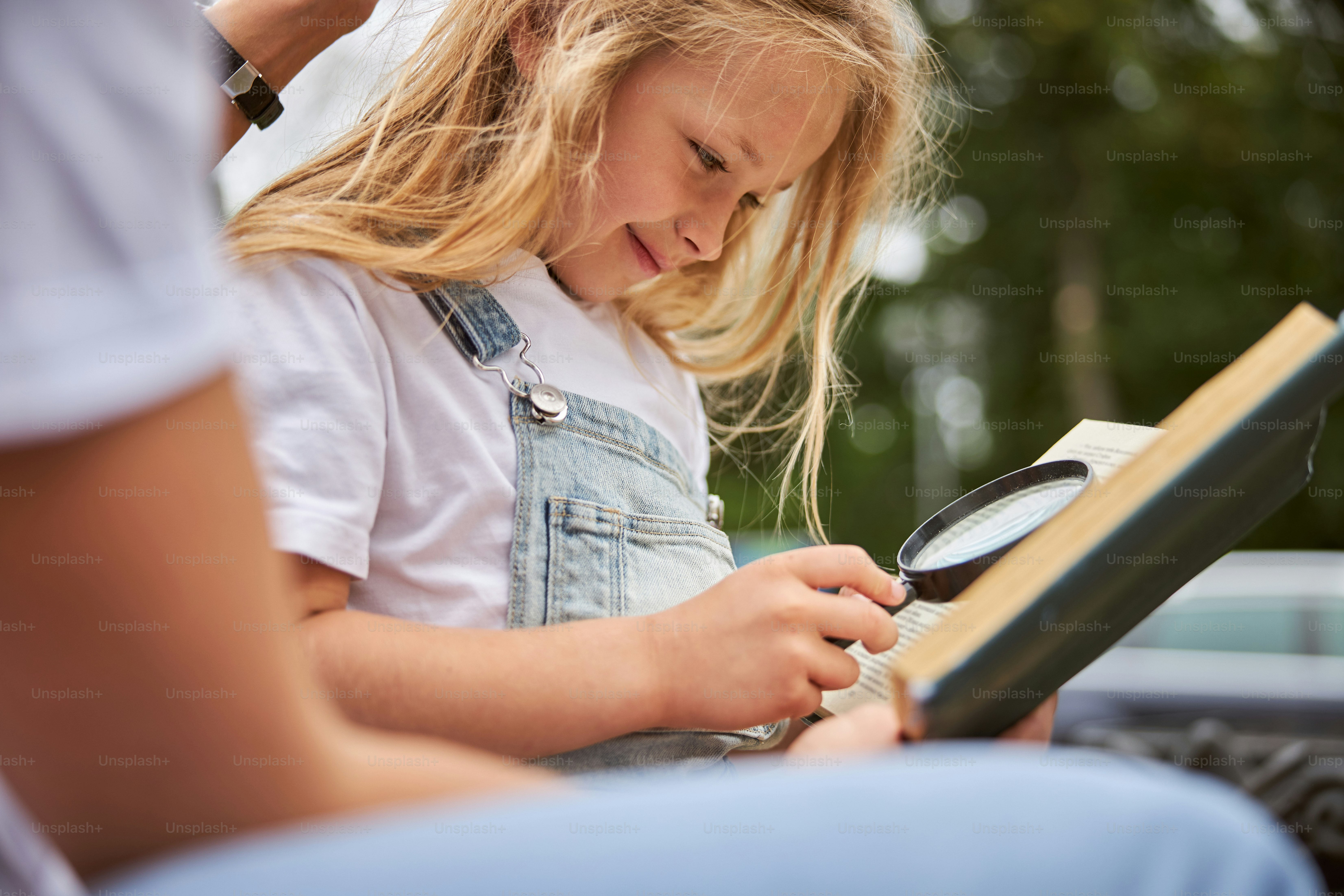 Gut aussehendes lächelndes Mädchen, das durch das Buch schaut und dabei die Lupe benutzt