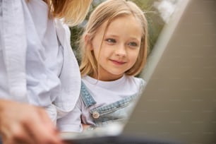 Cute charming young lady with grey eyes looking at the screen of laptop while sitting near the woman