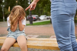 Porträt eines weinenden Mädchens mit Händchen auf der Bank im Stadtpark sitzend