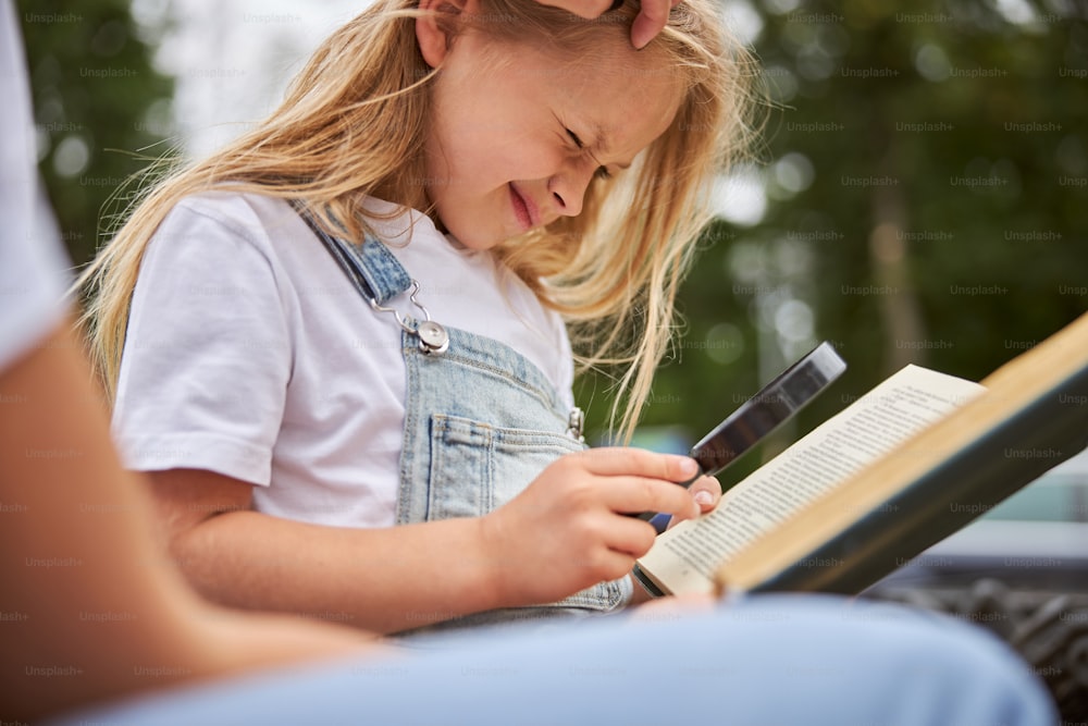 Happy smiling school girl holding magnifying glass in hand while sitting in the outdoors