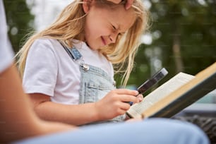 Happy smiling school girl holding magnifying glass in hand while sitting in the outdoors