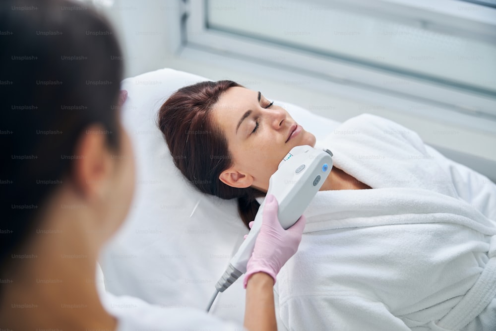 Serene middle-aged Caucasian woman with her eyes shut lying still during a non-invasive face-lift procedure