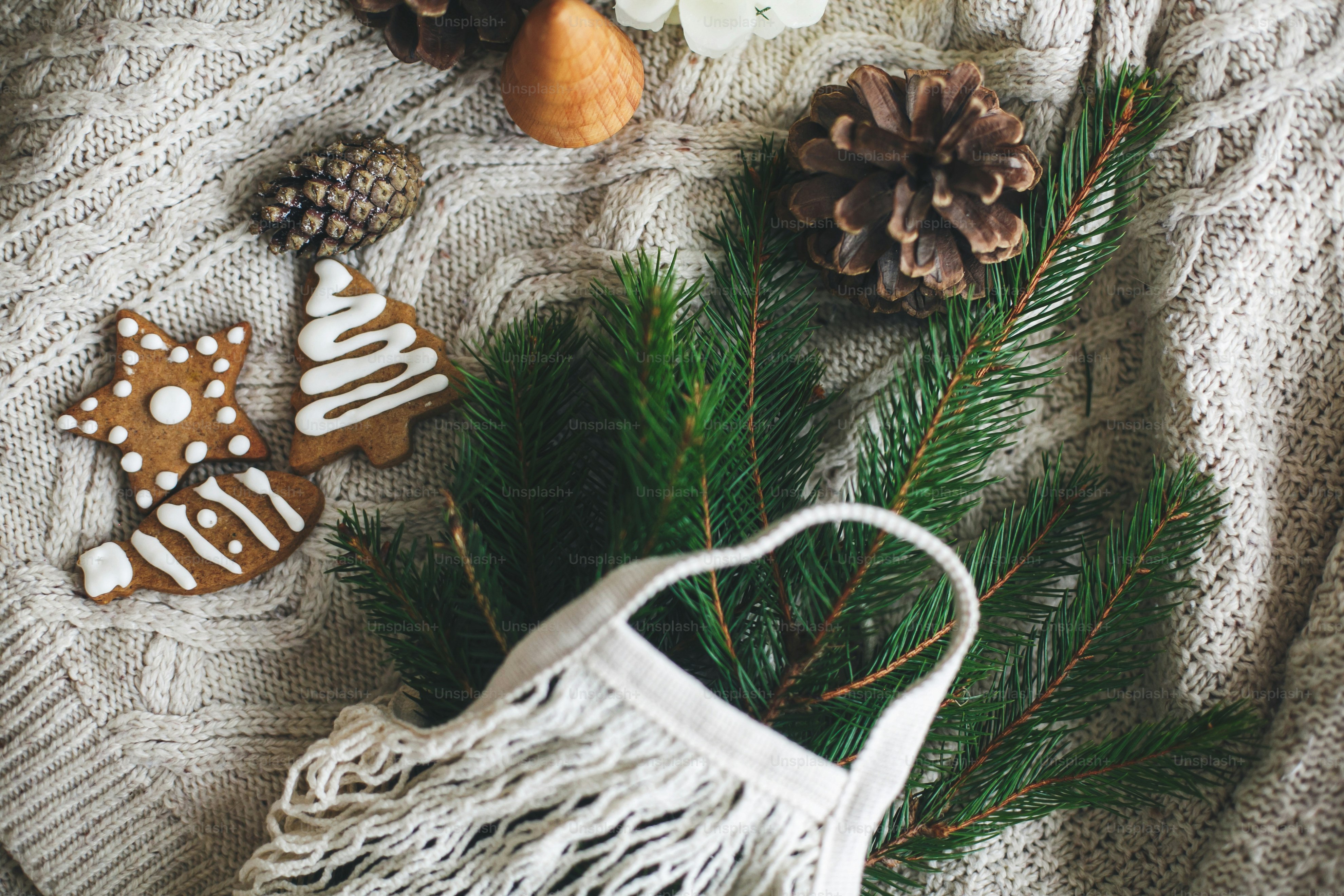 ゼロウェイストのクリスマス休暇。白いニットセーターに緑のトウヒの枝、ジンジャーブレッドのクリスマスクッキー、松ぼっくりが入った再利用可能なショッピングバッグ。プラスチックフリーの冬の装飾