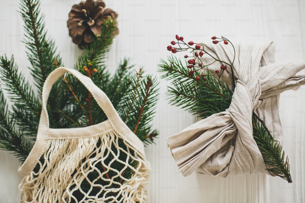 Vacances de Noël zéro déchet. Cadeau de Noël élégant enveloppé dans un tissu en lin avec une branche verte et un sac à provisions réutilisable avec de l’épicéa vert sur fond en bois rustique