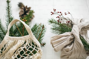 Elegante regalo de navidad envuelto en tela de lino con rama verde y bolsa de compras reutilizable con abeto verde sobre fondo de madera rústica. Vacaciones de Navidad residuo cero. Estilo de vida sostenible