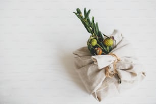 Vacances de Noël zéro déchet. Cadeau de Noël élégant enveloppé dans un tissu de lin et décoré d’une branche verte naturelle sur fond de table rustique blanc, espace pour le texte.