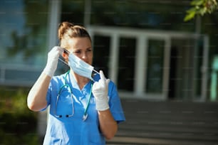 Pandémie de coronavirus. Femme médecin moderne en blouse avec stéthoscope et masque médical à l’extérieur près de l’hôpital.