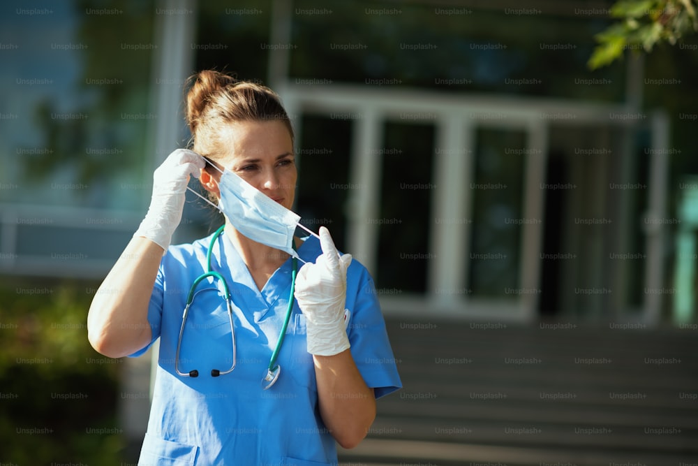 coronavirus pandemic. modern medical practitioner woman in scrubs with stethoscope and medical mask outdoors near hospital.
