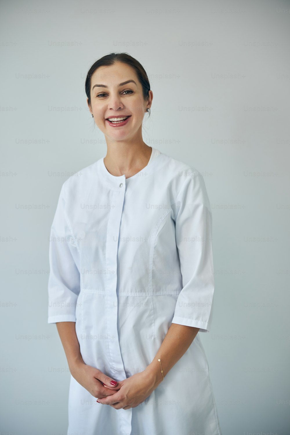 Front view of a cheerful cosmetologist dressed in a lab coat posing for the camera