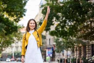 Young woman hailing a taxi ride. Beautiful charming woman hailing a taxi cab in the street. Businesswoman trying to hail a cab in the city. Tourist woman hailing a taxi