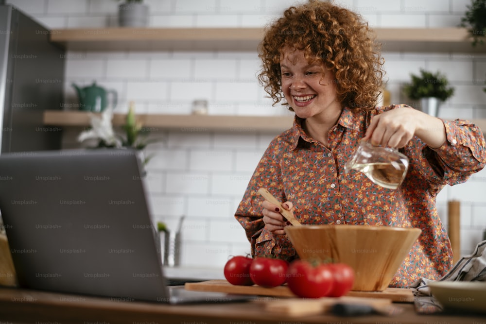 Young woman is reading a recipe while cooking. Beautiful woman with curly hair enjoying in the kitchen.