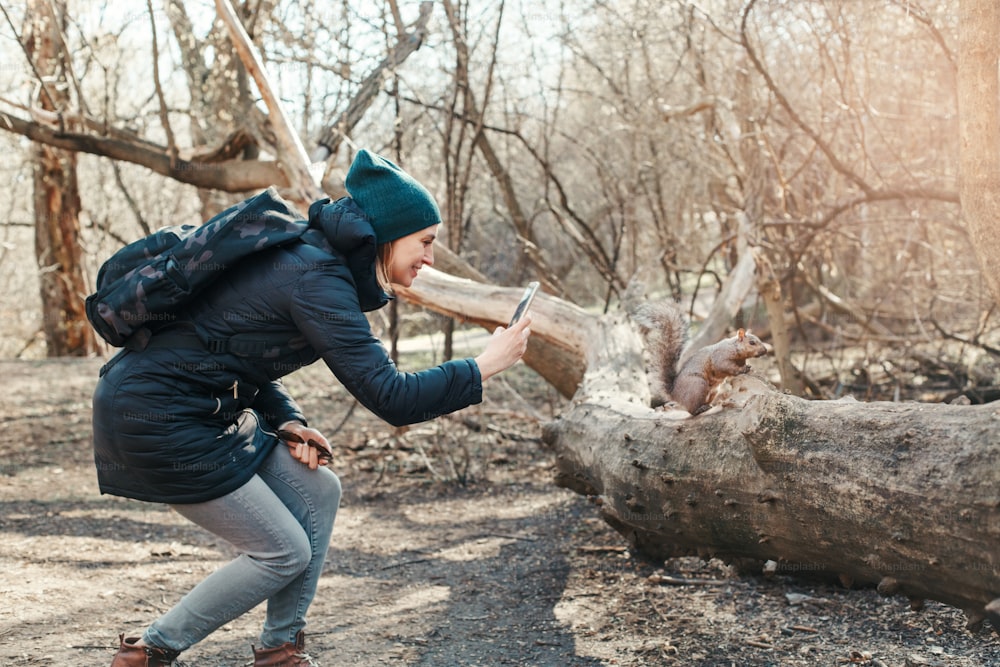 Donna caucasica che scatta foto di scoiattolo nel parco. Ragazza viaggiatrice turistica che scatta foto con lo smartphone di animali selvatici nella foresta. Divertente attività all'aperto e blogging vlogging online.