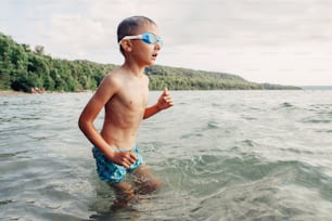 Caucasian boy swimming in lake river with underwater goggles. Child diving in water on beach. Authentic real lifestyle happy childhood. Summer fun outdoor aquatic recreational activity.