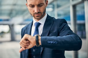 Besorgter junger Geschäftsmann mit gerunzelter Stirn, der auf seine Armbanduhr schaut und die Zeit überprüft