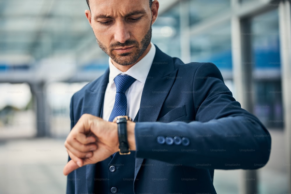 Worried young businessman with a furrowed brow looking at his wrist watch checking the time